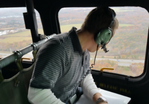 a helicopter passenger with a headset on looking out the fuselage window