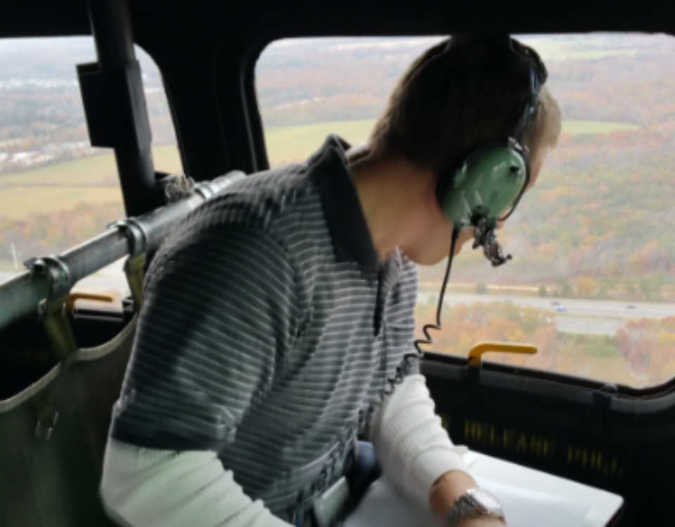 a helicopter passenger with a headset on looking out the fuselage window
